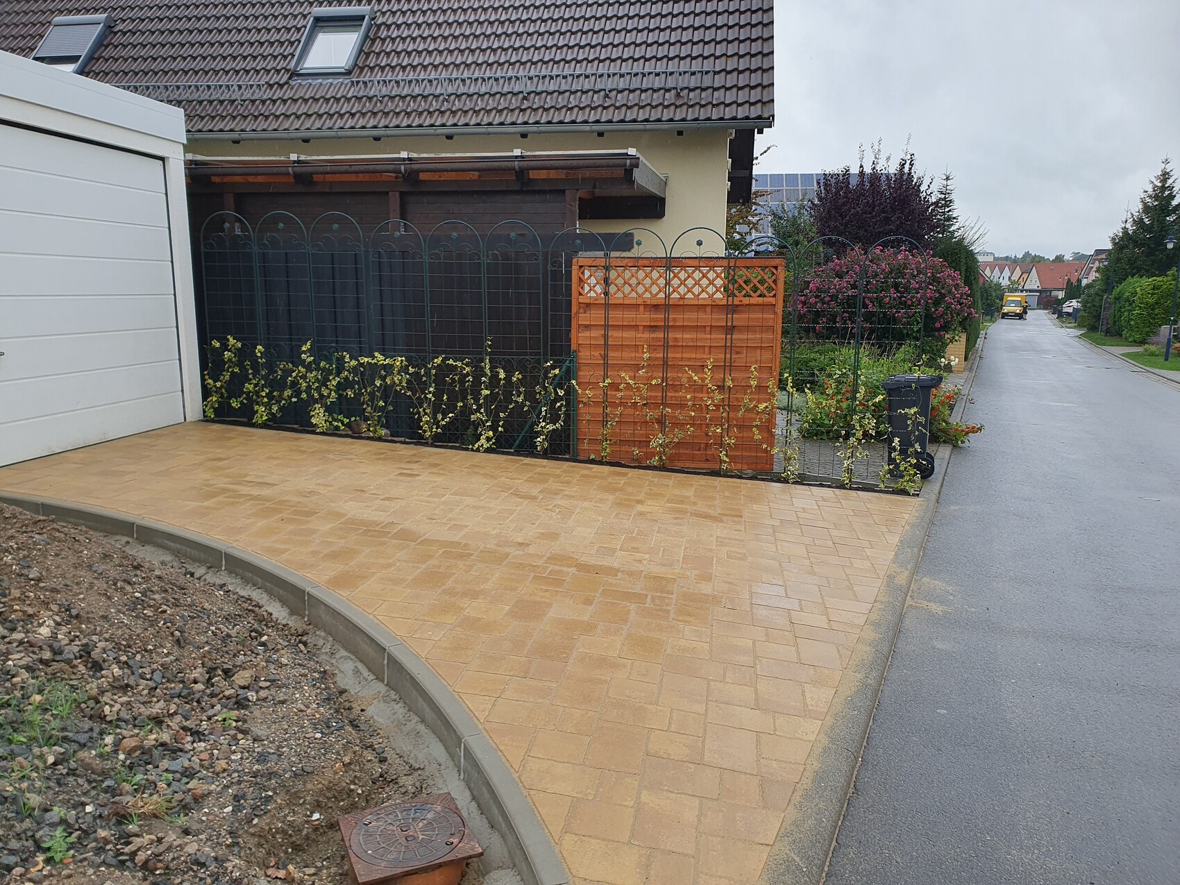 Vorderseite eines Hauses mit gepflasterter Terrasse, Zaun, Tor und Gartenpflanzen