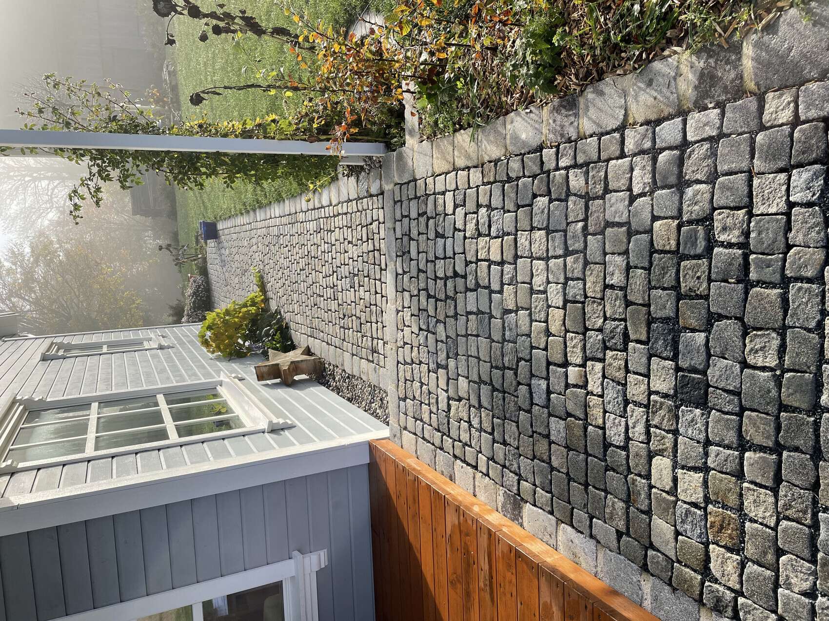 Gepflasterter Steinweg neben blau-grauem Haus mit Gartenpflanzen