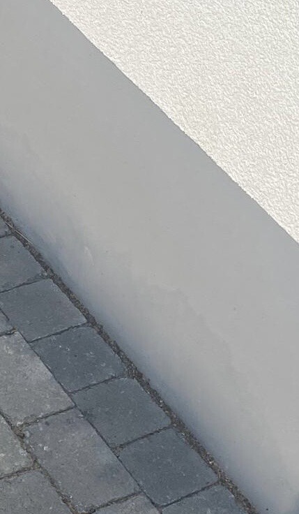Eckansicht: weiße, texturierte Wand trifft graue Wand über einem Pflasterweg.