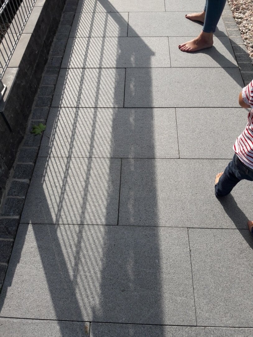 Gepflasterte Terrasse mit Schatten eines Geländers und barfuß spielenden Kindern
