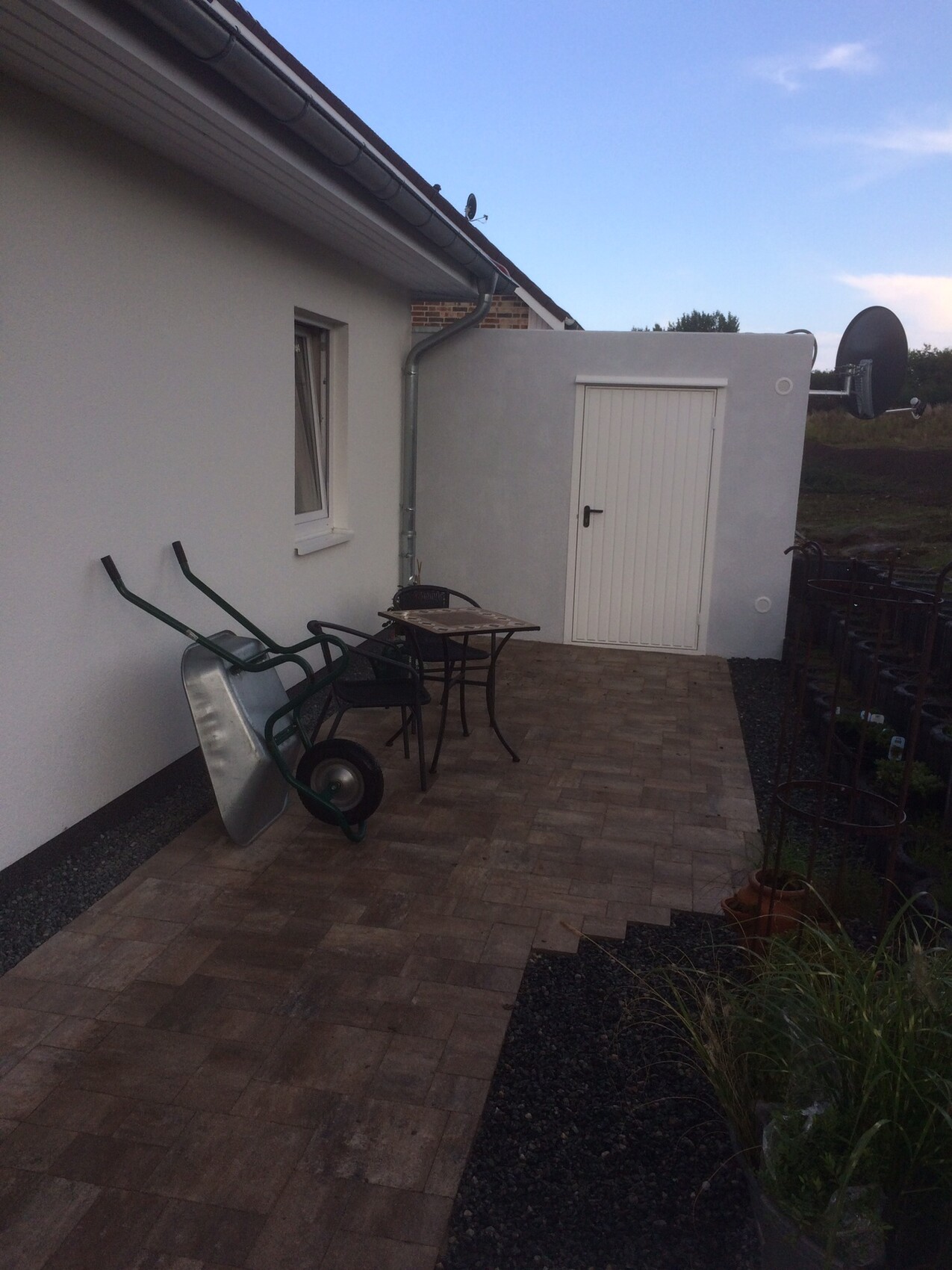 Patio neben einem Haus mit Tisch und Stühlen, Schubkarren, weiße Tür und Sat-Anlage.