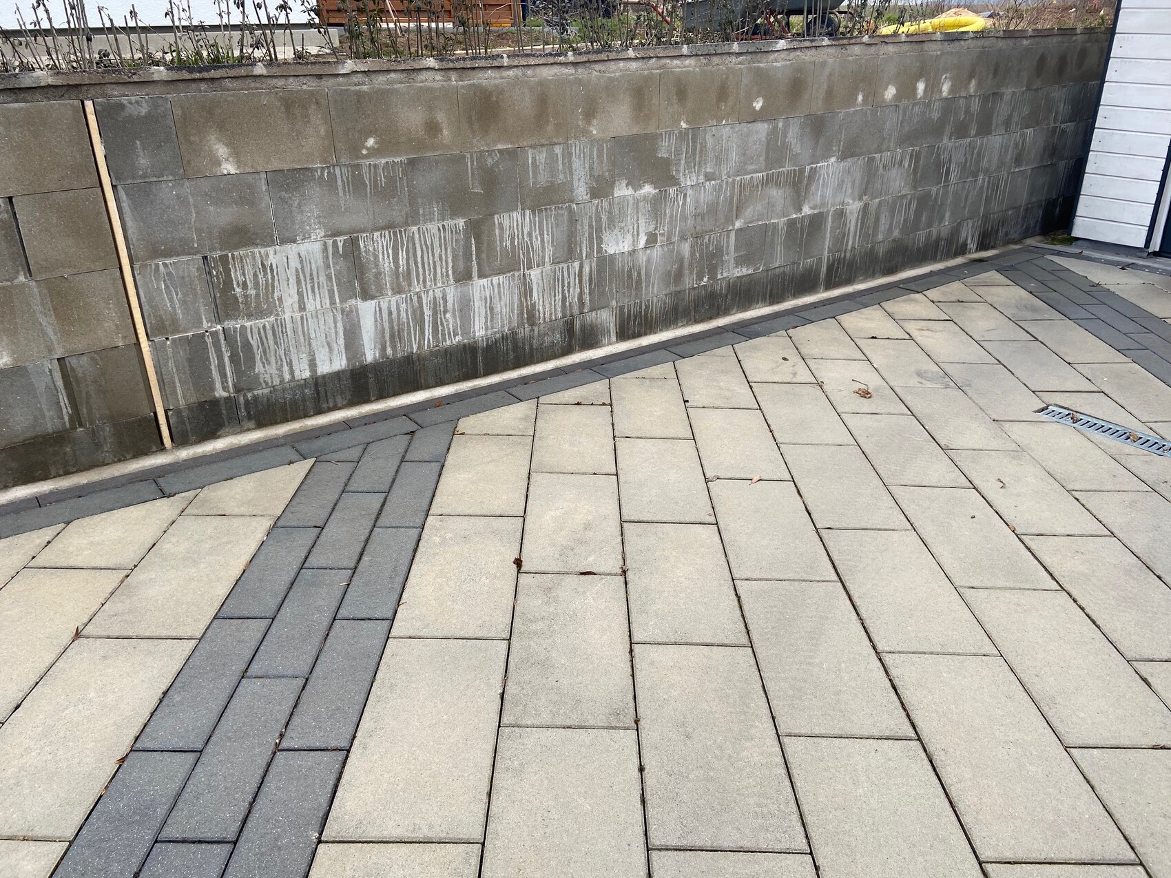 Gepflasterte Terrasse vor grauer Steinmauer; weiße Wasserflecken an der Wand, Rinne im Vordergrund.