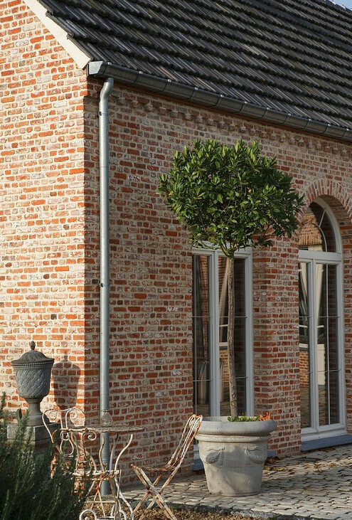 Rotbraune Ziegelhaus-Fassade mit Baum im Topf und Metall-Gartenmöbeln im Hof.