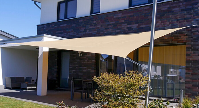 Außenansicht eines modernen Hauses mit großem beigem Sonnensegel über dem Patio und Gartenmöbeln.