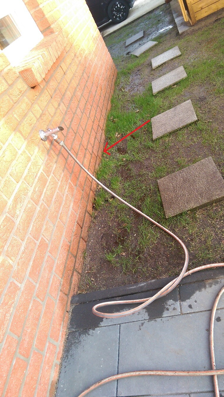 Außenbereich eines Hauses mit Steinplatten-Pfad, Grasflächen und Schlauch an der Wand