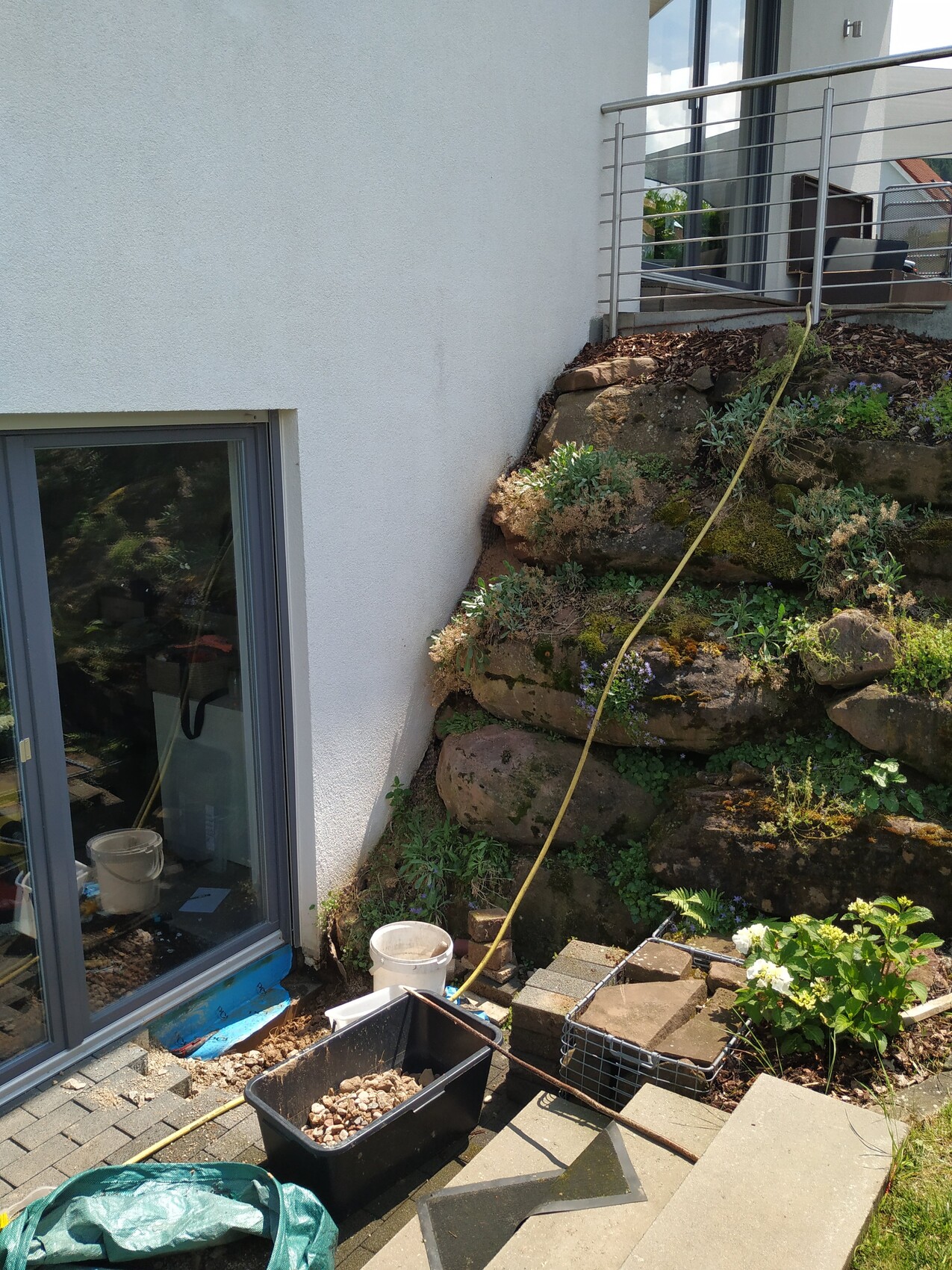 Außenansicht eines Hauses mit Glas-Schiebetür, Steinmauer und Gartengeräten im Baubereich