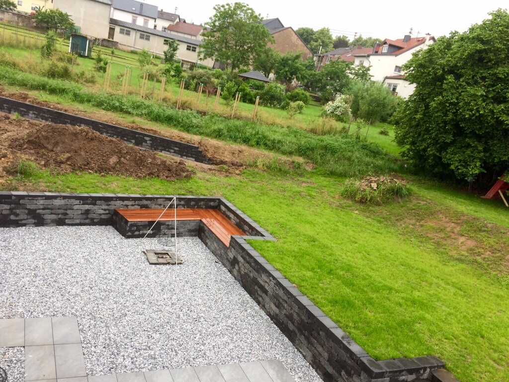 Gartenbereich mit terrassierter Steinmauer, Kiesfläche und Holzbank im Hof