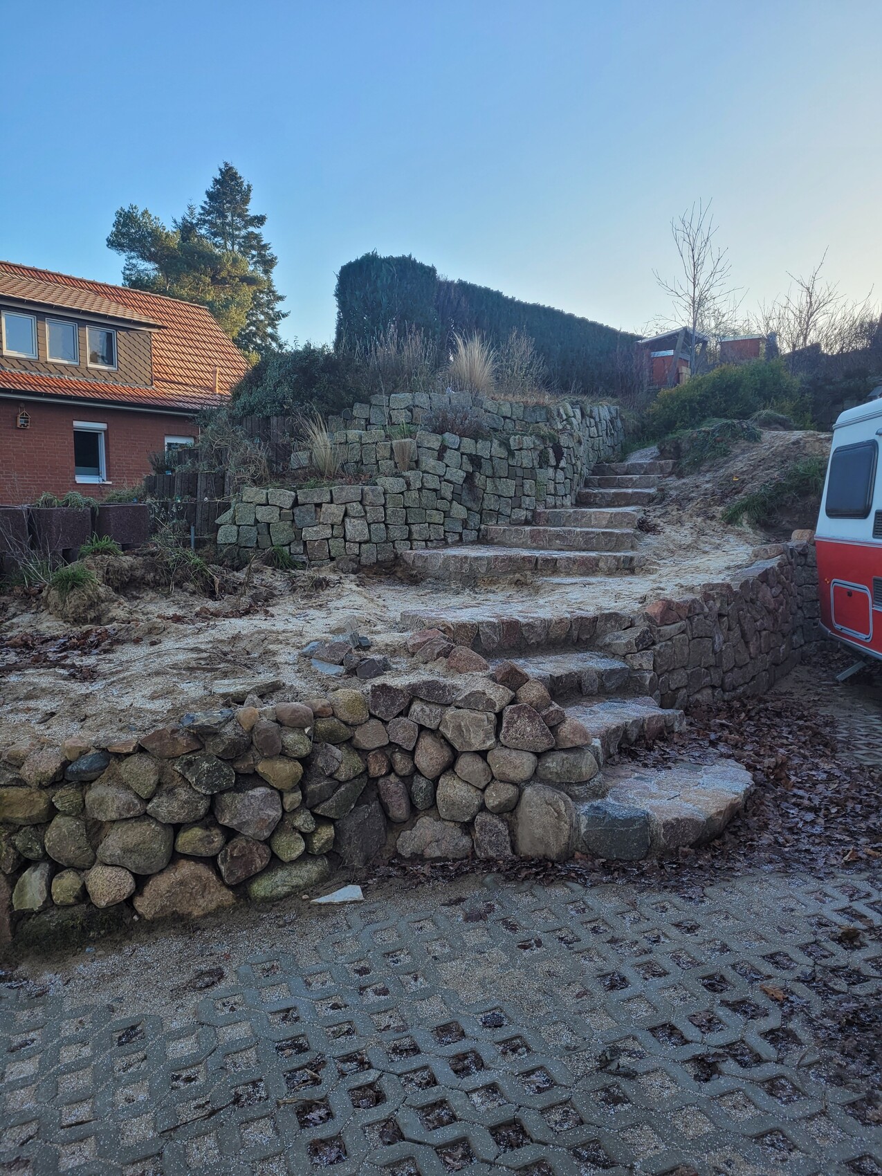 Naturstein-Treppen und Trockenmauer vor Haus mit rotem Ziegeldach; Wohnwagen rechts.