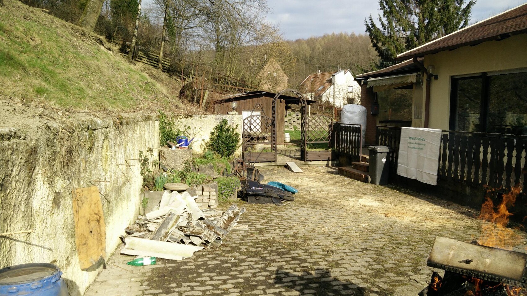 Garten- und Terrassenbereich mit Steinpflaster, Zaun, Laube und Bauabfaelle.