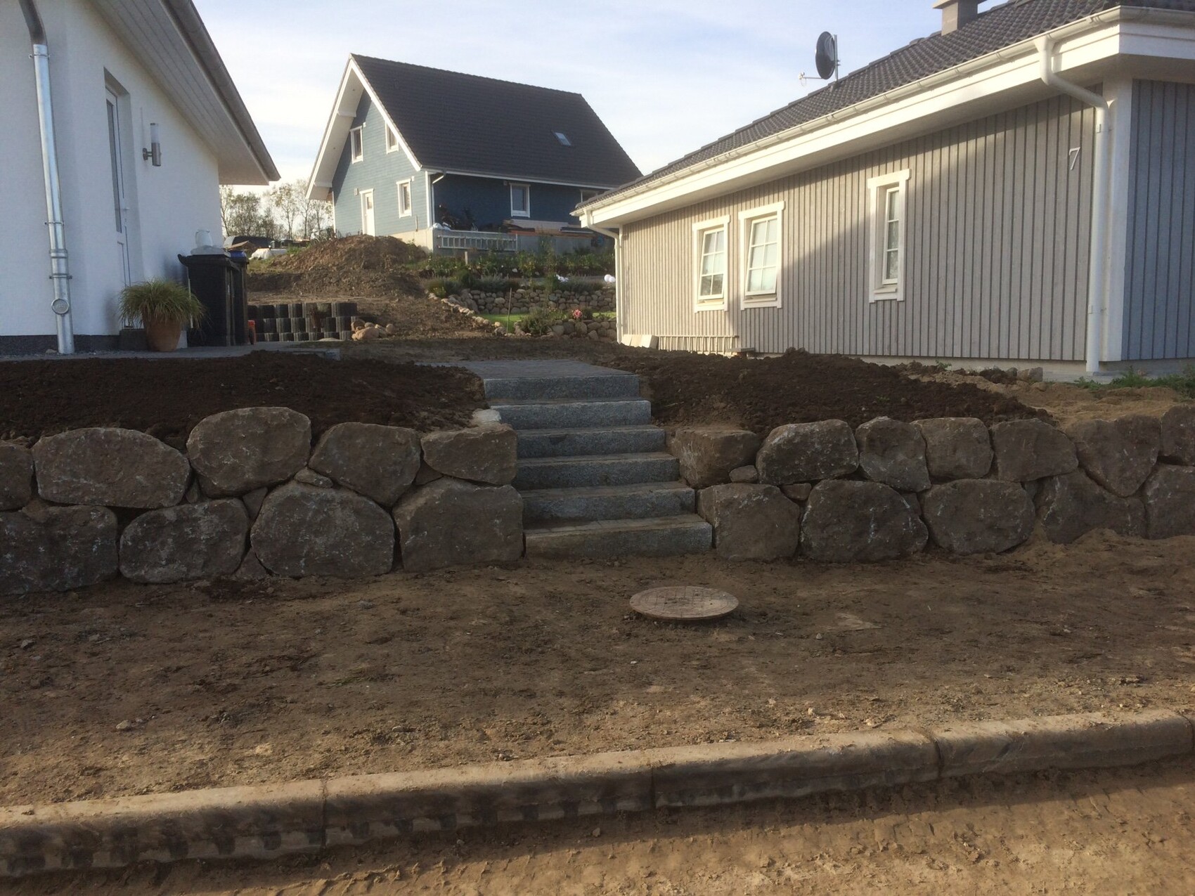 Außenansicht: Steinmauer, Stufen und Erdarbeiten im Gartenbereich.