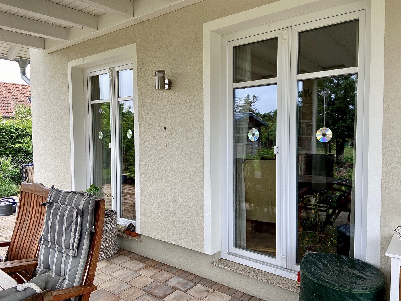 Veranda vor Haus: Zwei weiße Glasschiebetüren, Holzstuhl, Pflanze, CDs an den Fenstern.