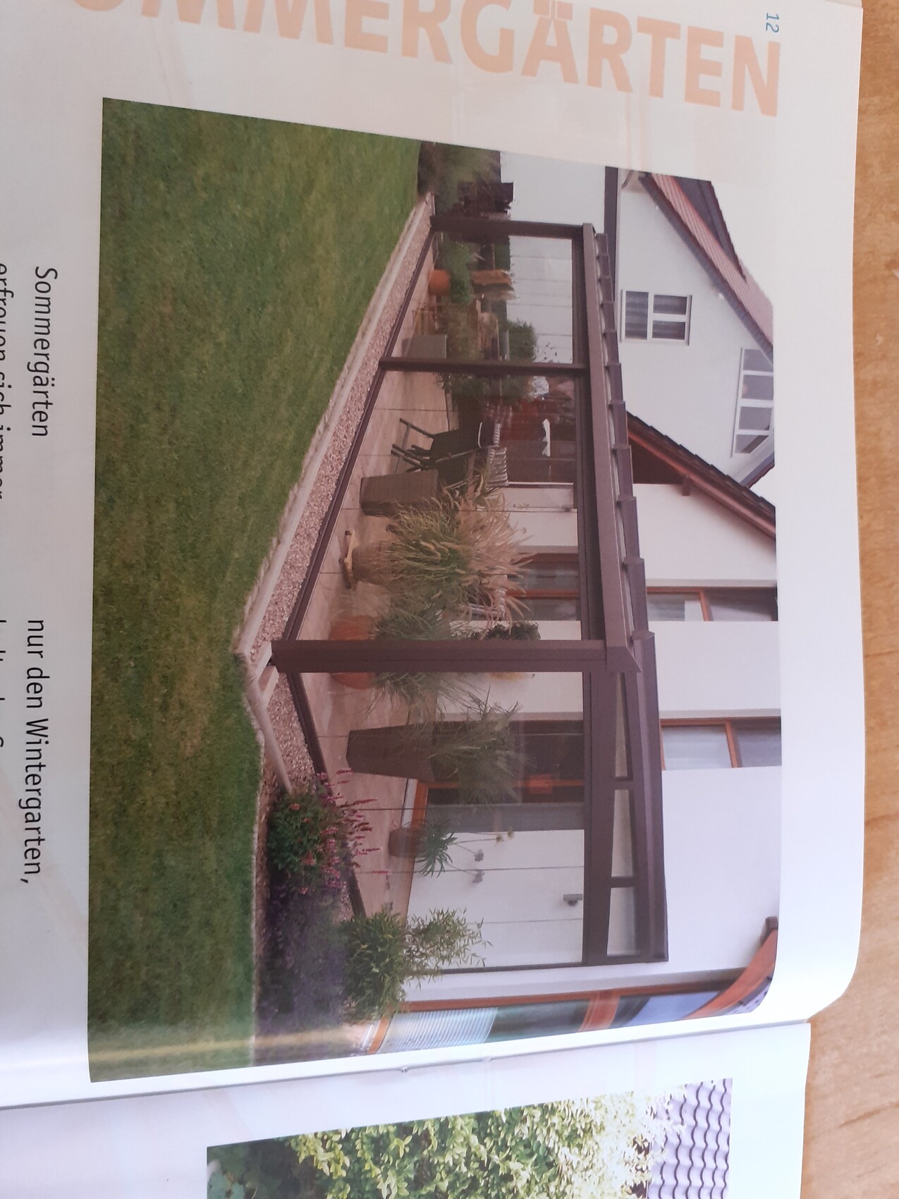 Terrassenveranda am Haus mit dunklem Rahmen, Topfpflanzen und grünem Garten davor.