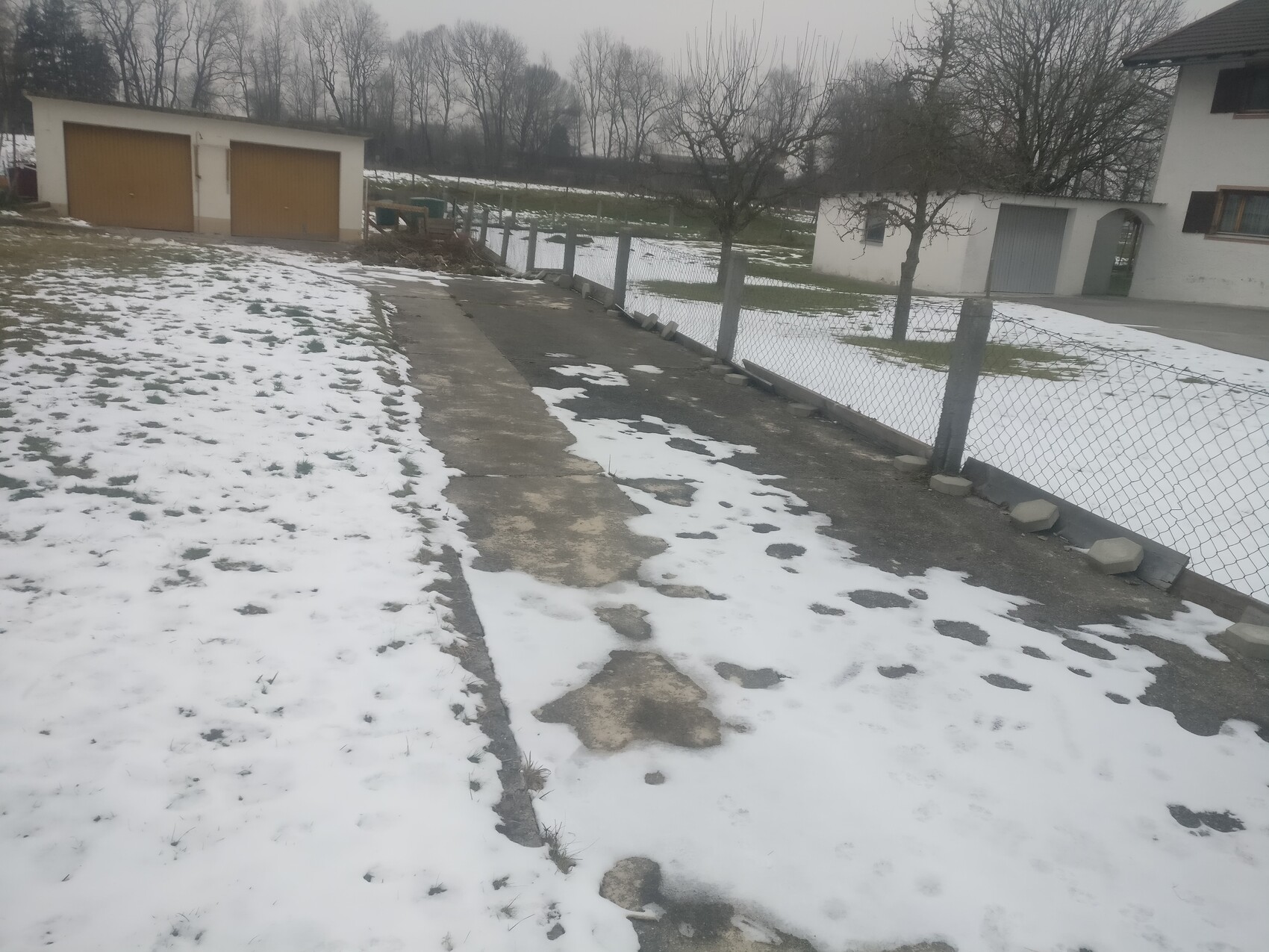Außenansicht eines Wohnhauses mit Garage, Einfahrt, Zaun und schneebedecktem Vorplatz im Winter