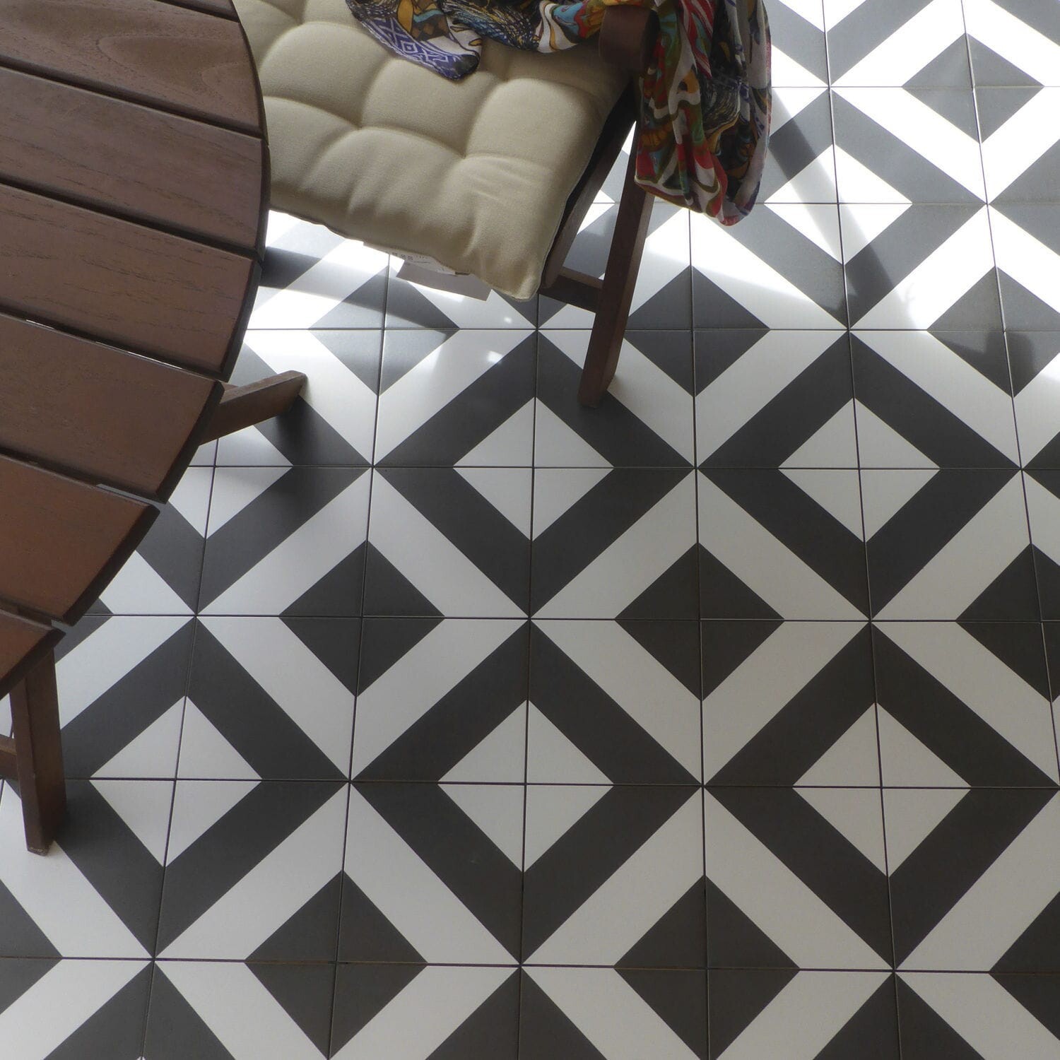 Geometrische schwarz-weiße Terrassenfliesen mit runder Holztisch und gepolstertem Stuhl.