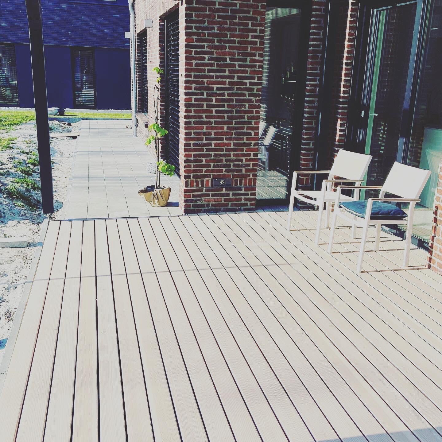 Terrasse aus Holzplanken neben Backsteinwand; zwei weiße Stühle mit Kissen