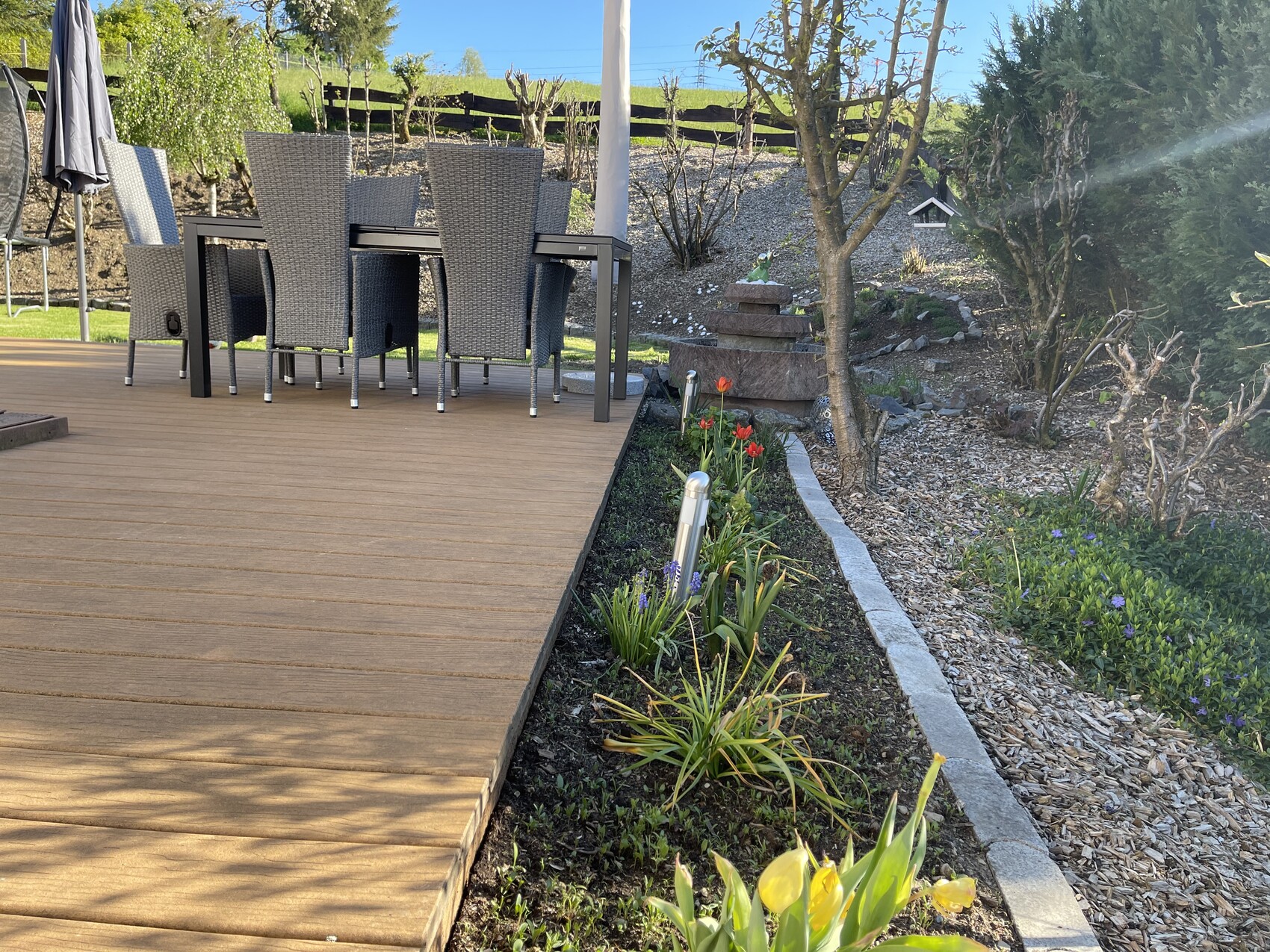 Holzdeck mit Esstisch und Stühlen, Tulpenbeet und gepflegter Gartenweg.