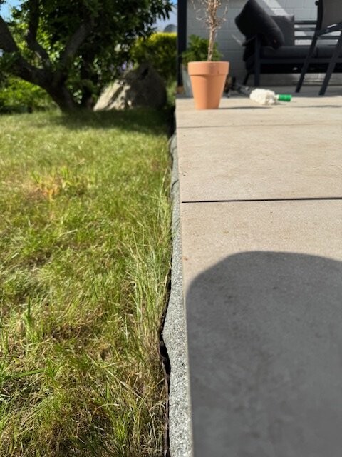Riss in der Betonkante neben Gras; Terracotta-Topfpflanze und Flasche auf Terrasse