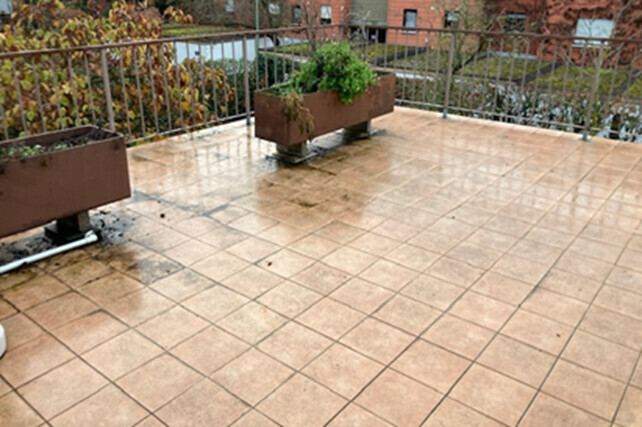 Blick auf eine begehbare Terrasse mit hellen Fliesen, Pflanzkübeln und Geländer