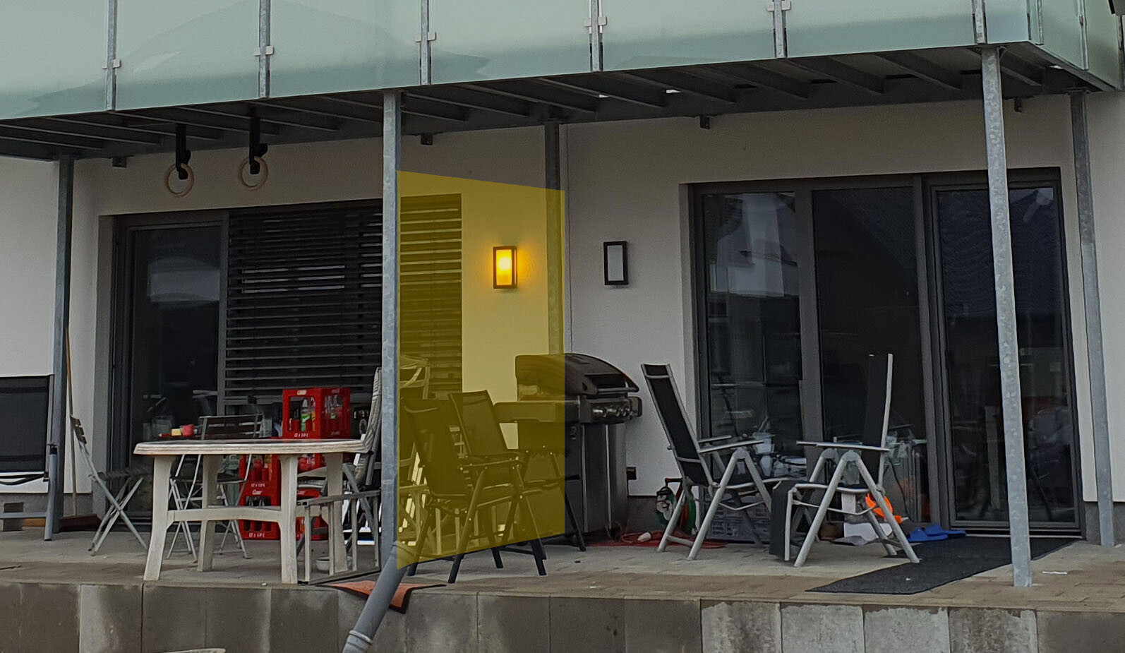 Terrassenbereich vor modernem Haus: Grill, Outdoor-Tisch, Stühle, Glastüren, gelb getönte Scheibe.