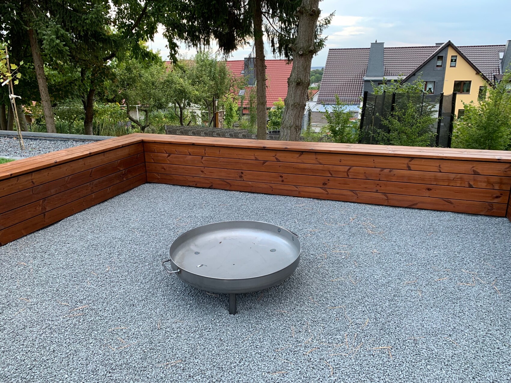 Dachterrasse mit Kiesboden, Holzverkleidung und runder Feuerschale in der Mitte.