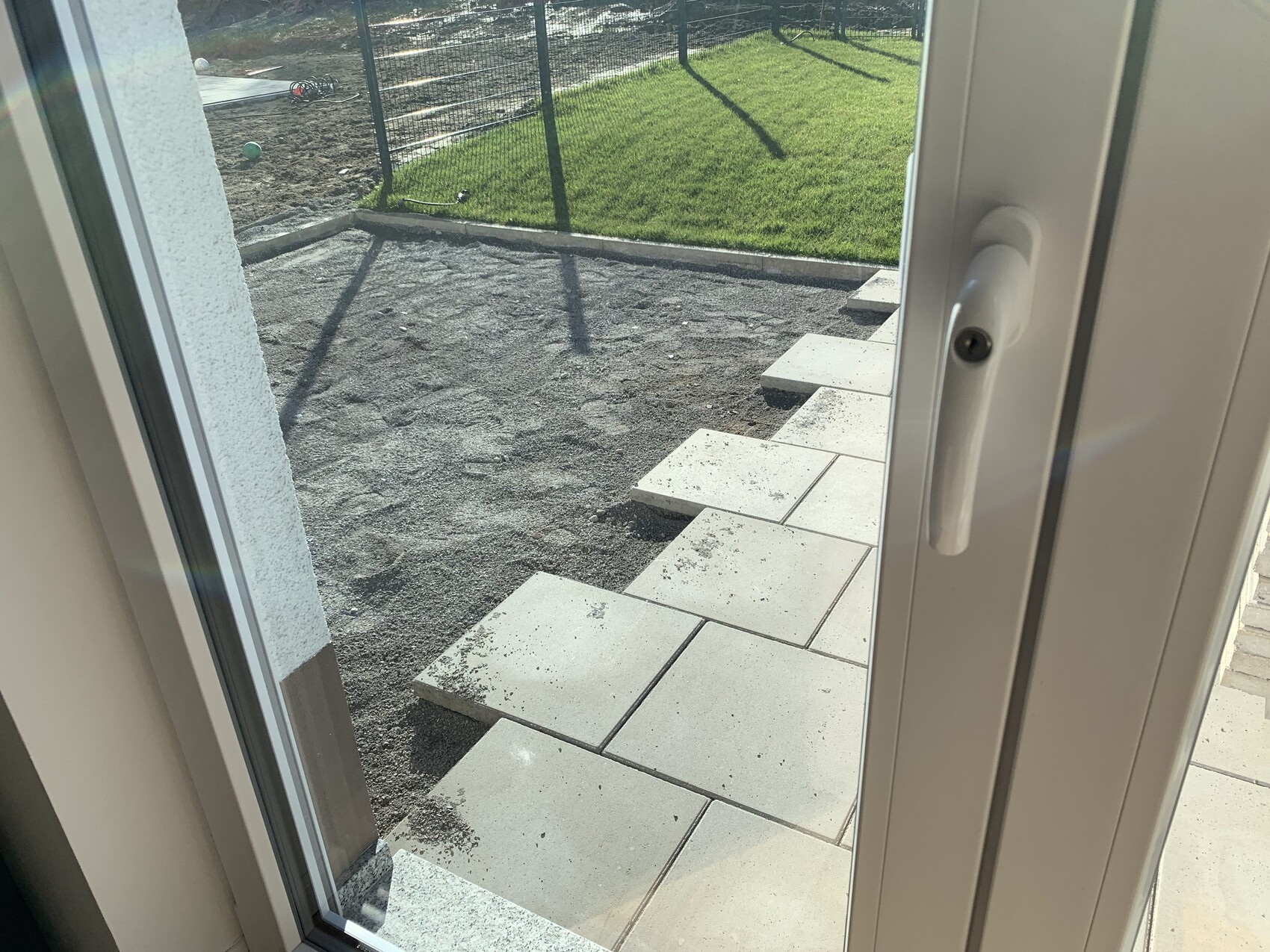 Blick durch Glastür auf Treppen aus Pflastersteinen zum grasbewachsenen Garten hinter Zaun.