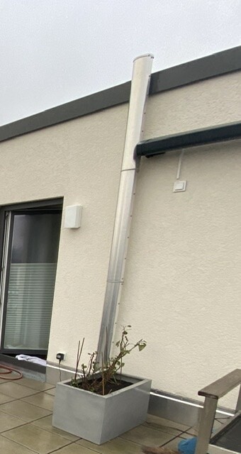 Außenansicht einer Terrasse mit senkrechtem Regenrohr, Pflanzkübel und Fenster
