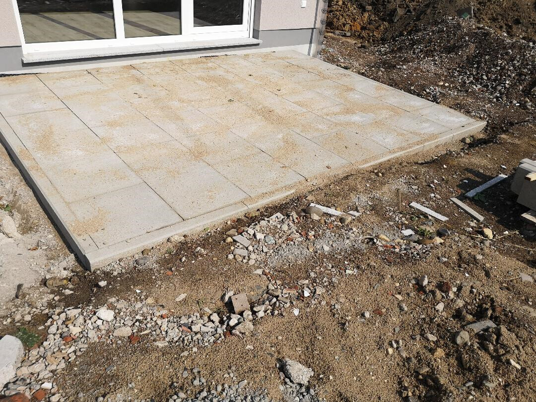 Neue Beton-Terrasse neben dem Haus, umliegende Erde und Bauabfall sichtbar.