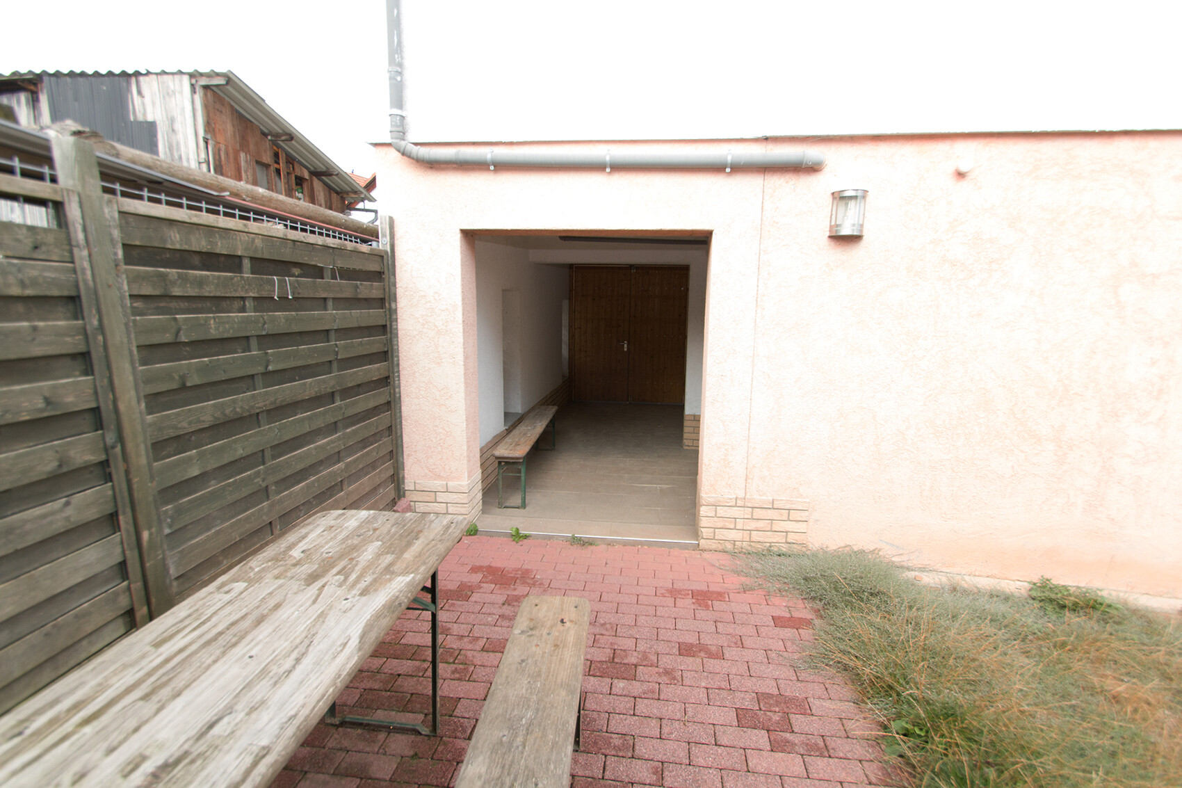 Außenterrasse mit rosa Wand, offener Eingang, Holzbank und Holzzaun auf Pflasterstein
