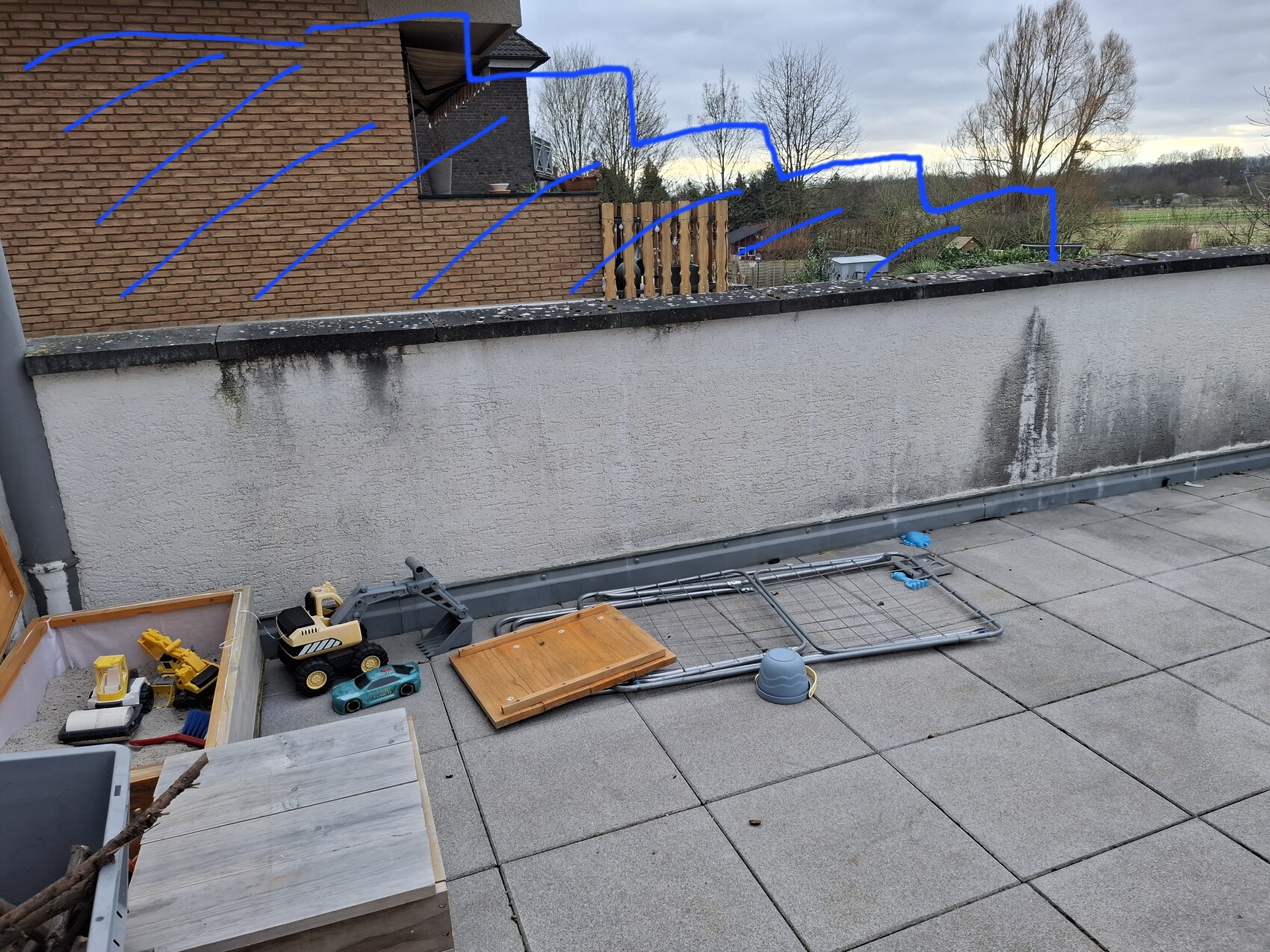 Auf einer Dachterrasse liegen Spielzeugautos, eine Holzkiste, ein Metallgestell und Kleinteile.