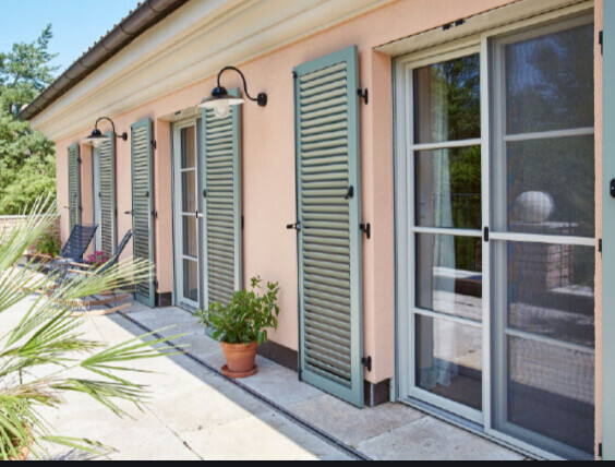 Außenansicht eines Hauses mit Terrassentüren, grünen Fensterläden und Topfpflanze.