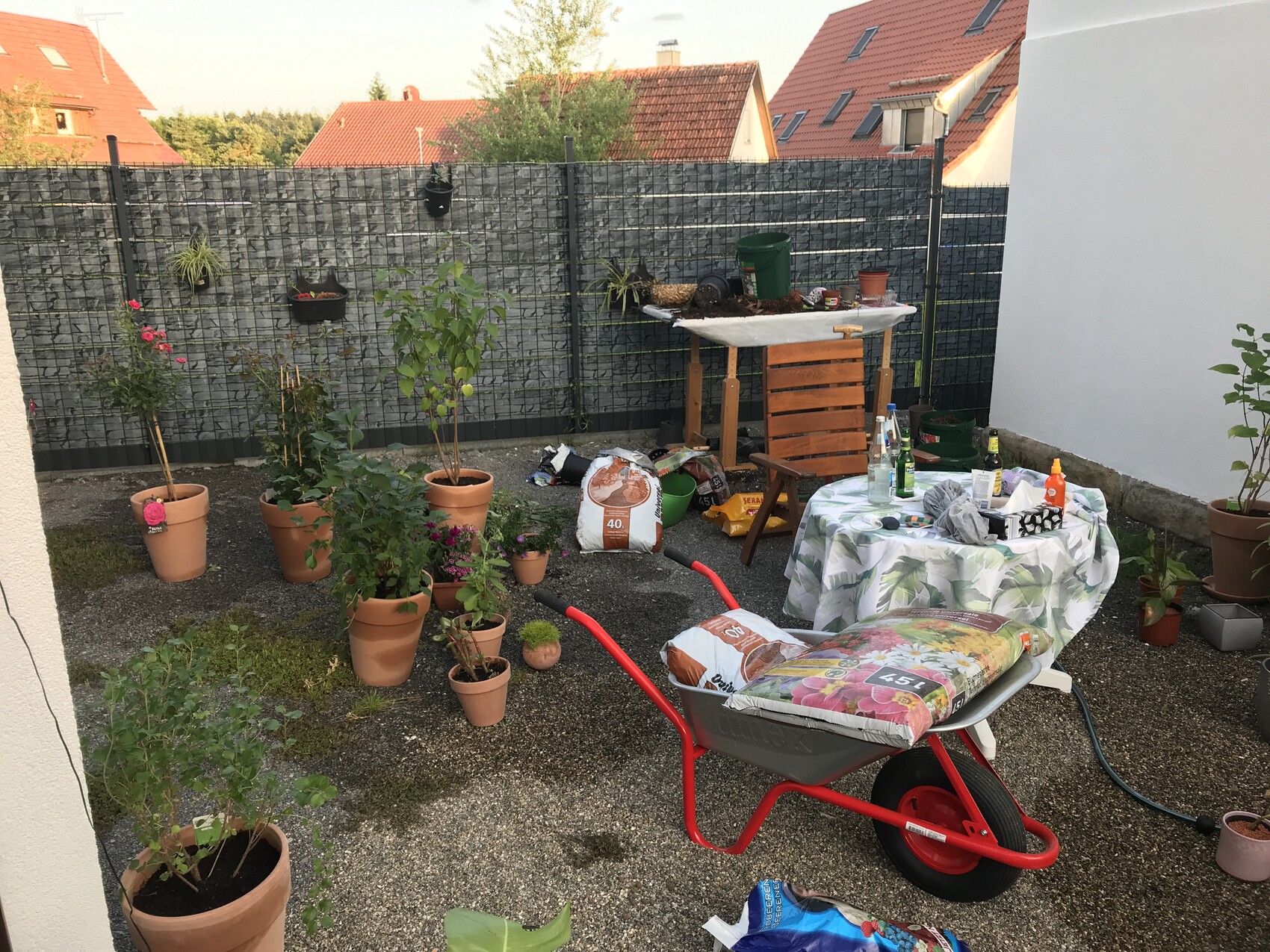 Hinterhof-Garten mit vielen Blumentöpfen, Schubkarre und einem Tisch mit Gartenutensilien.