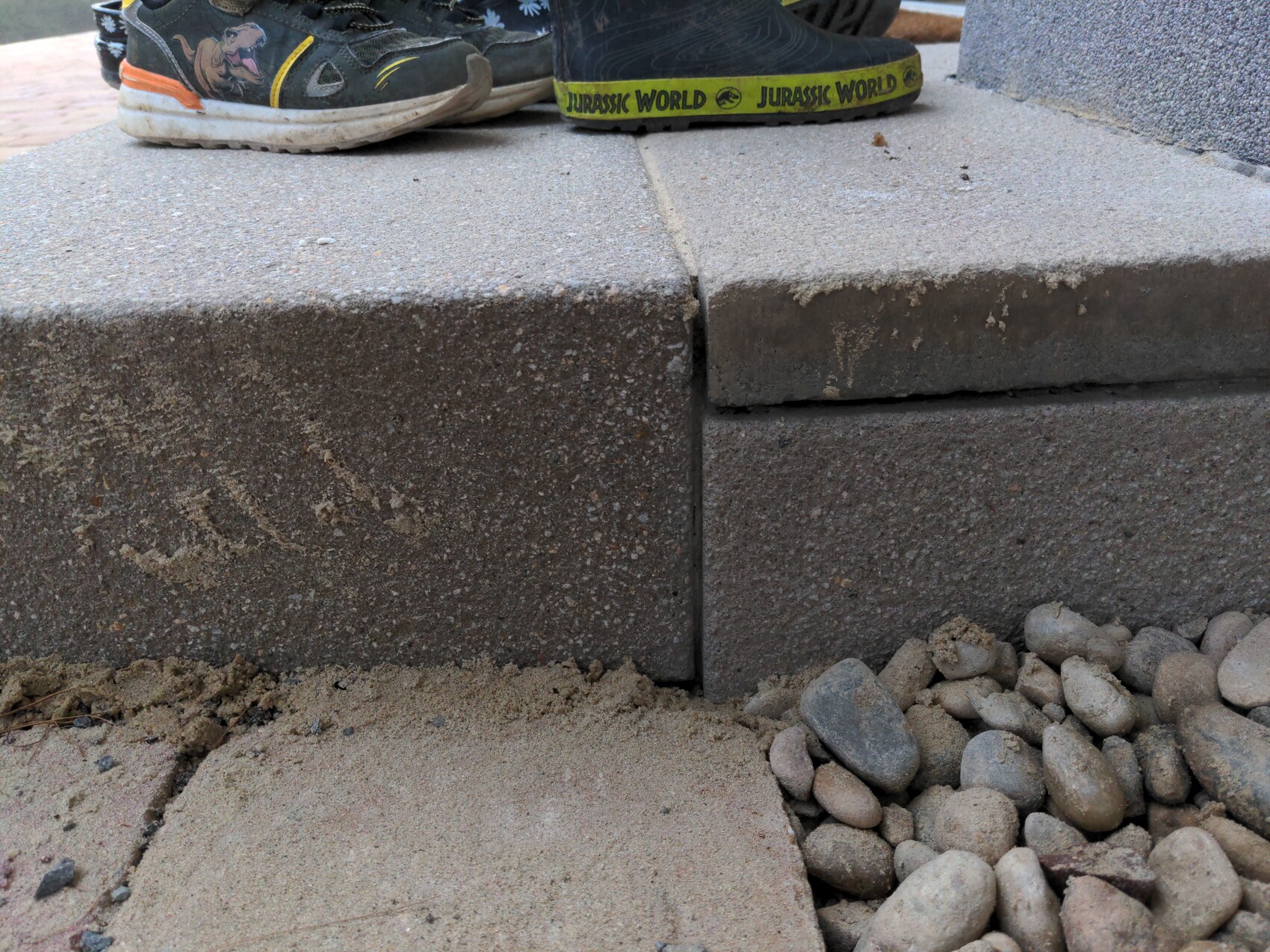 Sneaker steht auf Betonstufen, Lücke zwischen Blöcken, Kiesel am Rand.