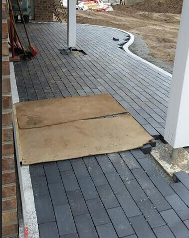 Außenbereich: dunkle rechteckige Pflastersteine als Terrassenweg, Holzplatten liegen darauf.