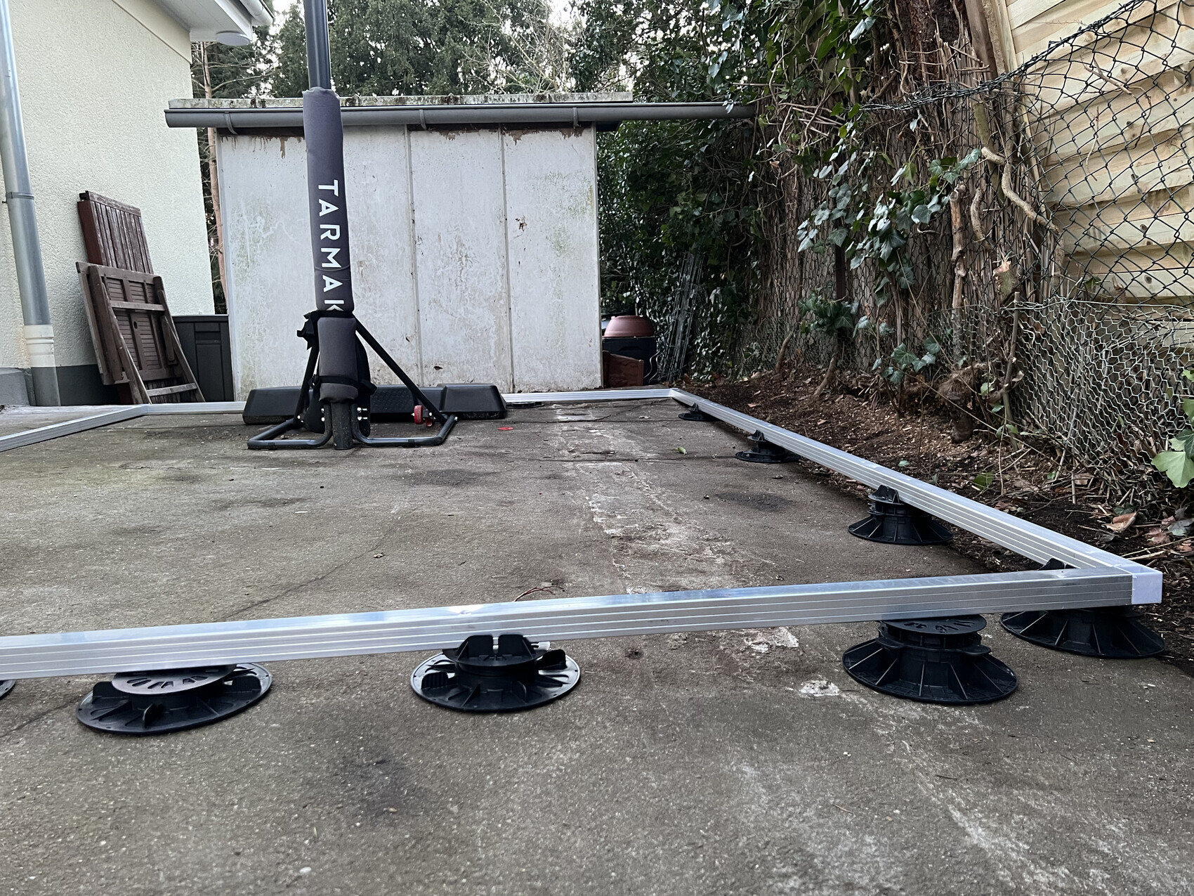 Zerlegter Trampolinrahmen mit großen schwarzen Standfüßen auf Betonfläche.