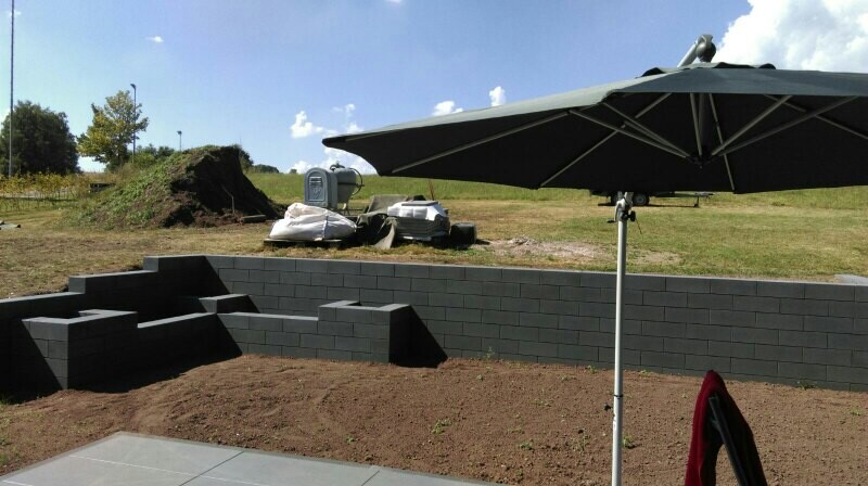 Außenbereich mit gestapelten grauen Betonblöcken als Stützmauer, Terrasse und Sonnenschirm.