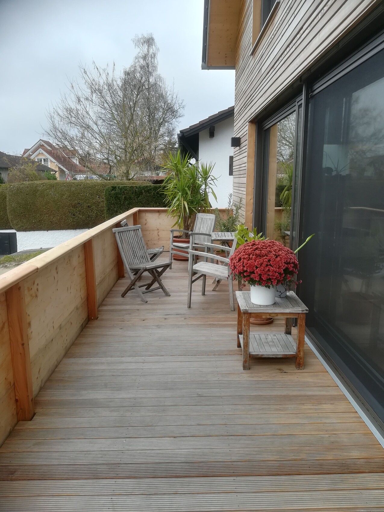 Holzterrasse mit Balkonmobiliar, Pflanzentopf und Glasschiebetür.