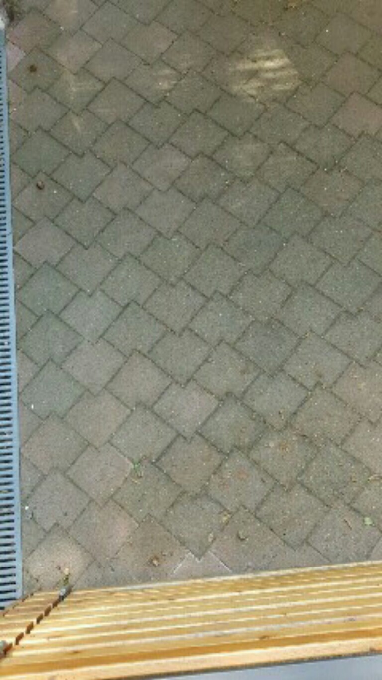 Gepflasterte Terrasse aus quadratischen Pflastersteinen, linke Messlatte sichtbar, Holzkante am unteren Rand