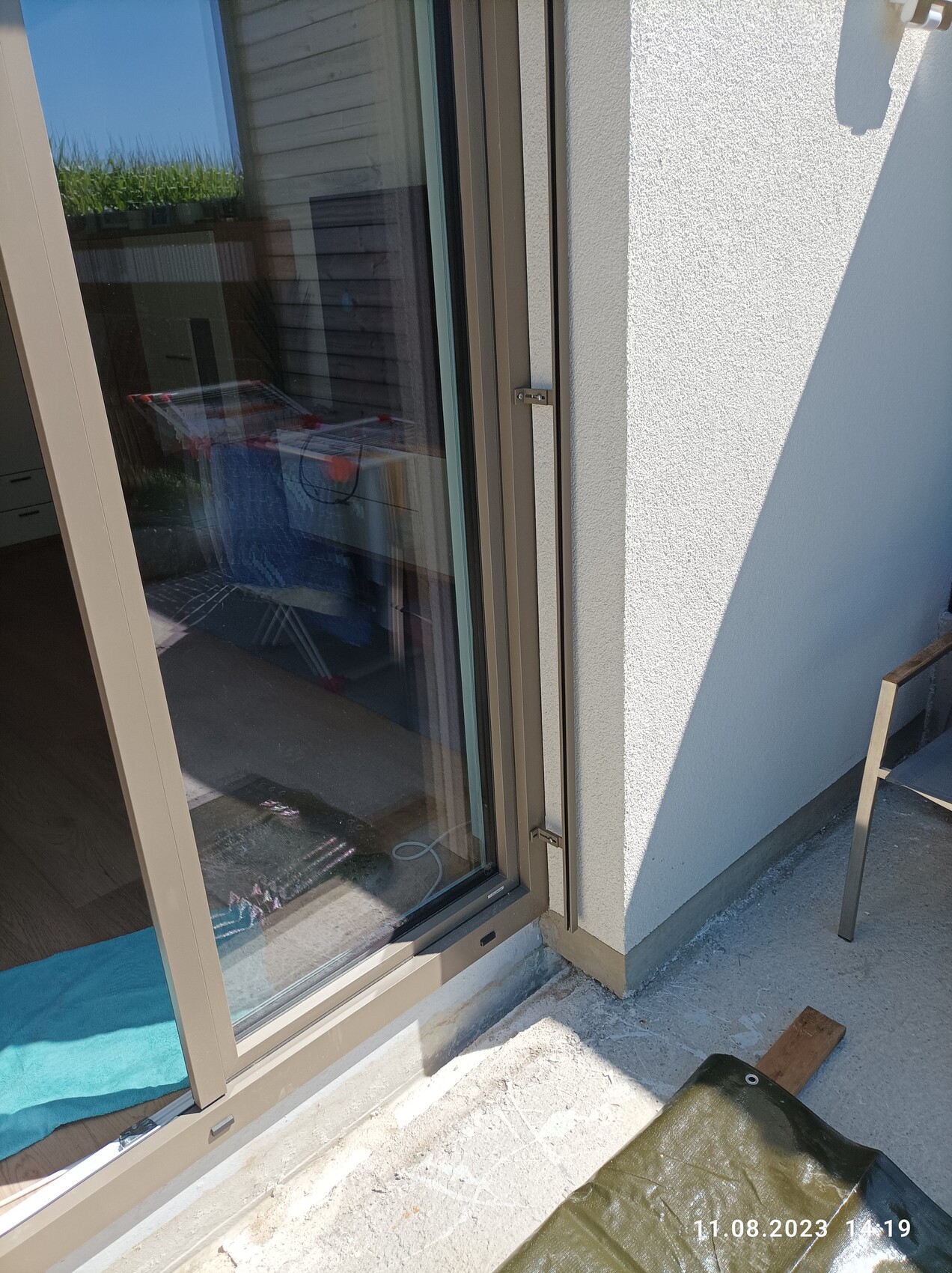 Terrassentür mit beigeem Rahmen an weisser Aussenwand; Innenraum sichtbar, blaues Handtuch davor.