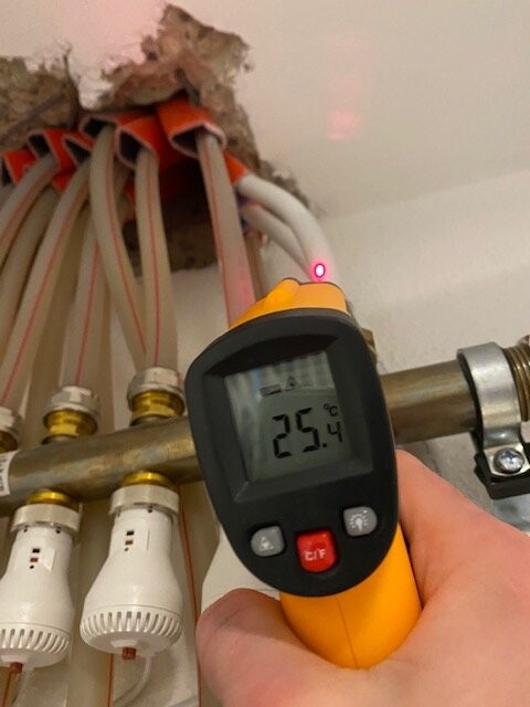 Infrarot-Thermometer misst an Rohren 25,4°C; Hand hält das Messgerät.