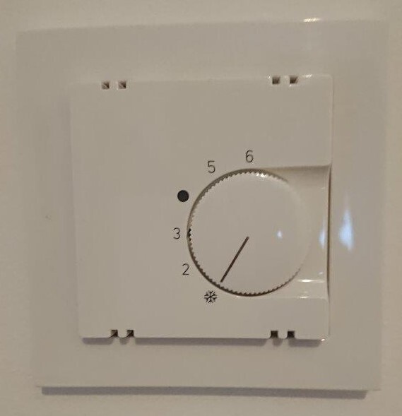 Weißer Thermostat-Drehknopf an der Wand mit Skala 2–6; Zeiger zeigt grob Richtung 4.