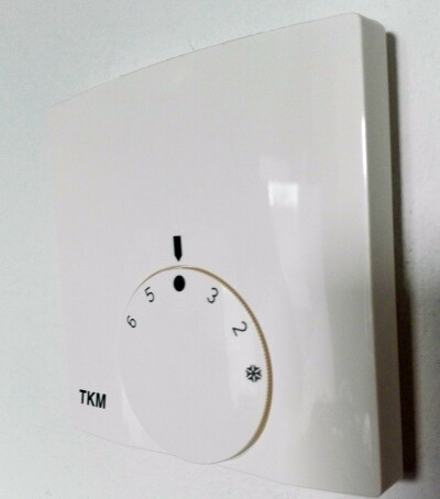Weißer Wandthermostat mit Drehknopf zur Heizungsregelung.