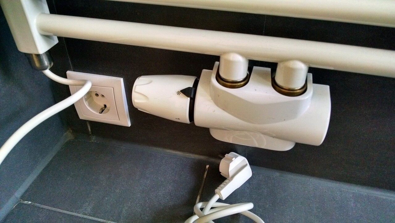 Weißes Thermostatventil am Heizkörper mit Steckdose und losem Kabel