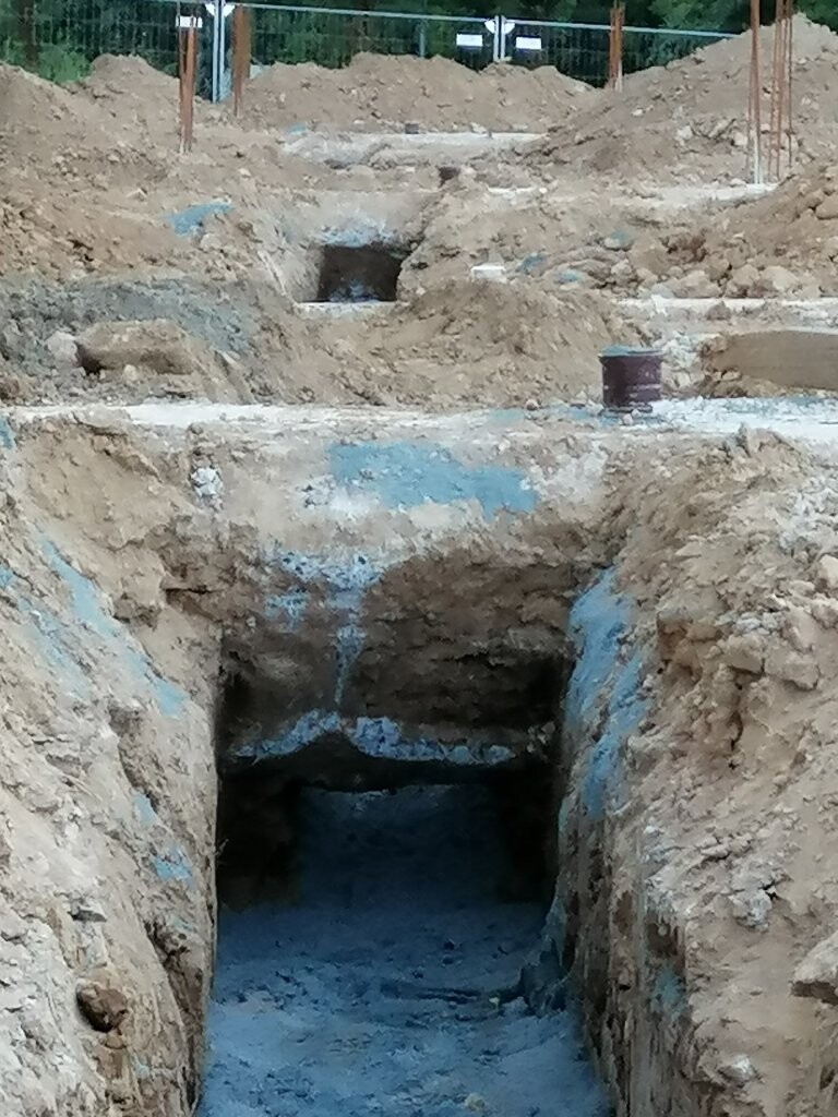 Baustellen-Grube mit erdigem Rand, blaue Betonflächen, dunkler Boden.