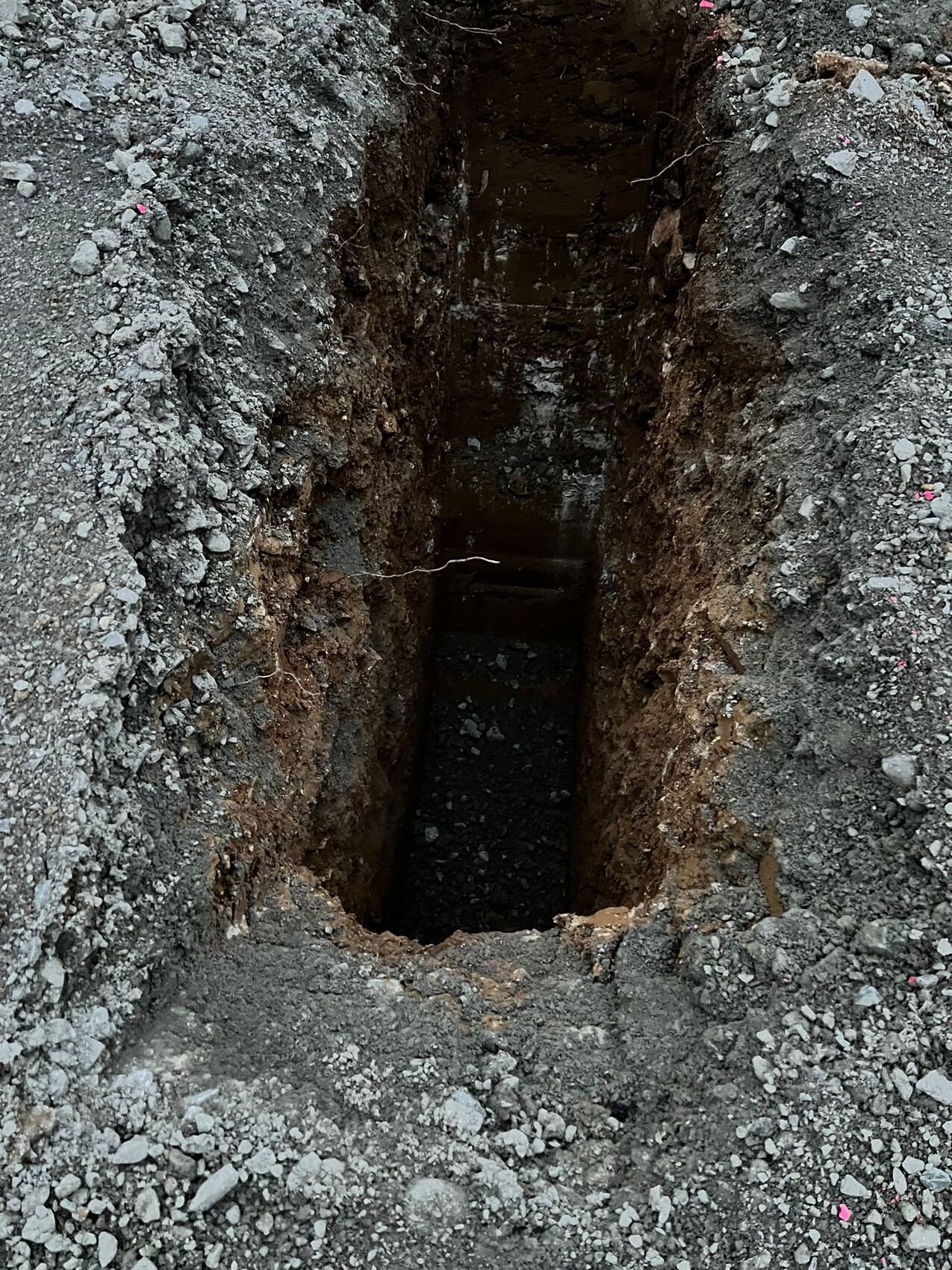 Vertikaler Erdschacht mit steiniger Wandung; dunkler Innenraum sichtbar.