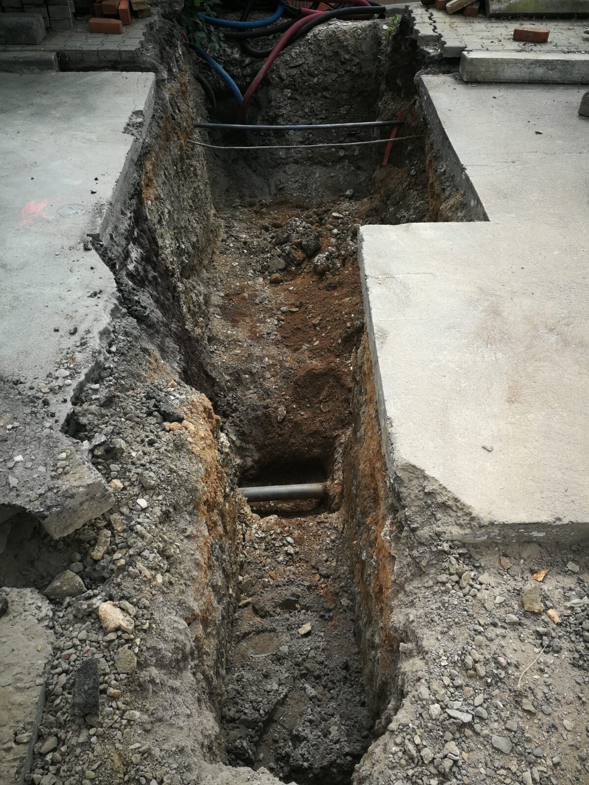 Offener Baugraben mit rohrförmiger Leitung, losem Erdreich und Betonplatten seitlich