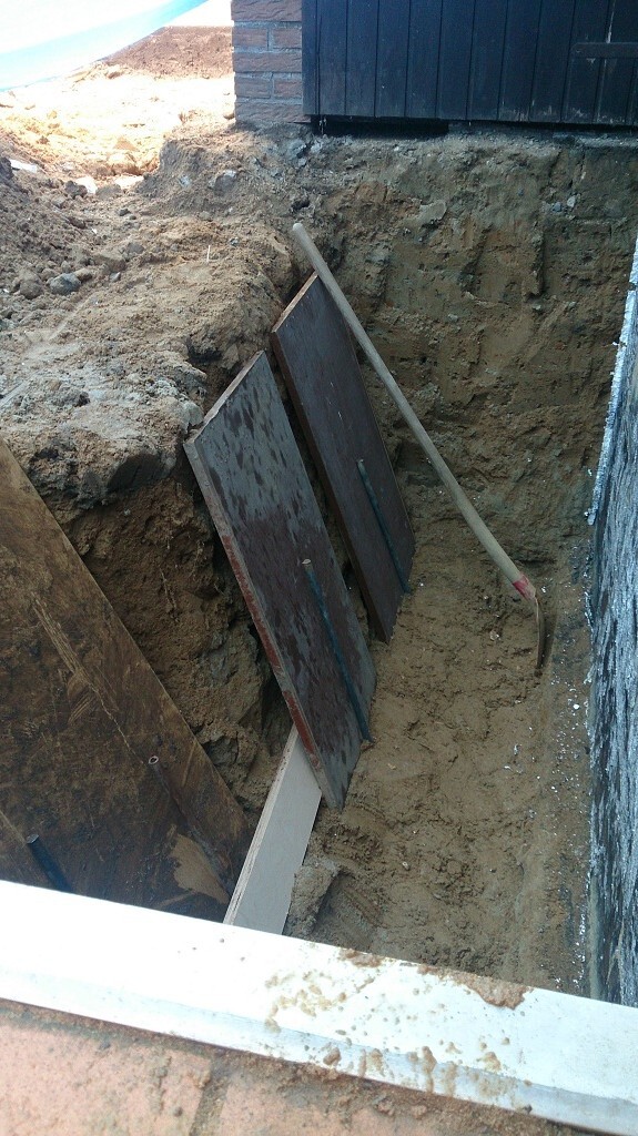 Tiefes Baugrubenfeld neben Hausfundament mit Holzbohlen und Sandboden