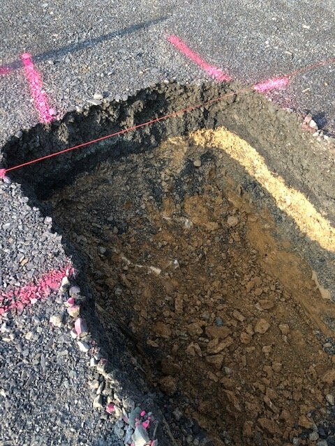 Grube im Asphalt mit lockerem Erdreich und pinken Markierungslinien am Rand