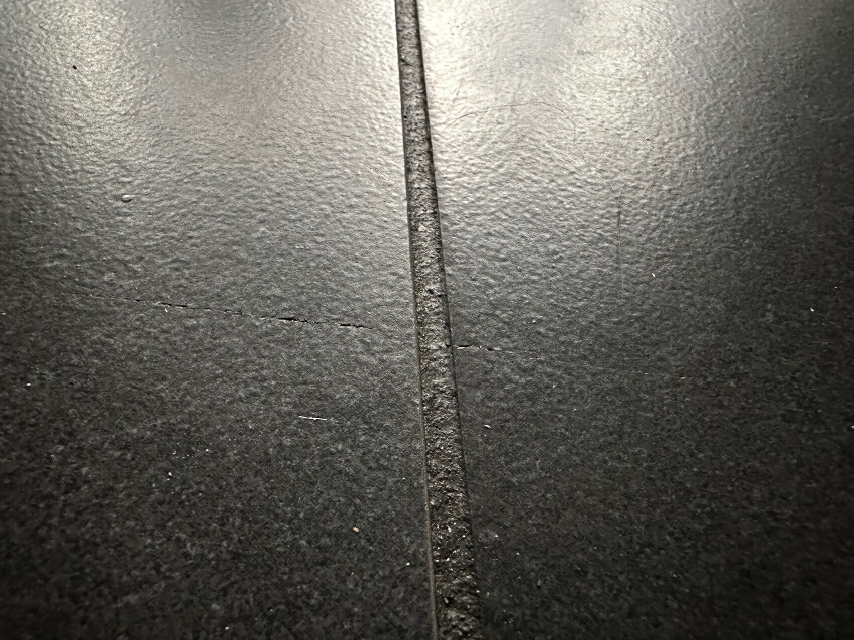 Dunkle, grob texturierte Bodenplatten mit einer schmalen vertikalen Fuge in der Mitte.