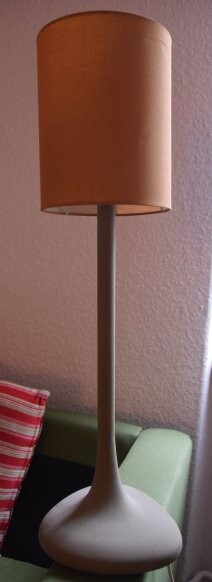Tischlampe mit orangefarbenem Lampenschirm vor grünem Sofa im Wohnzimmer.