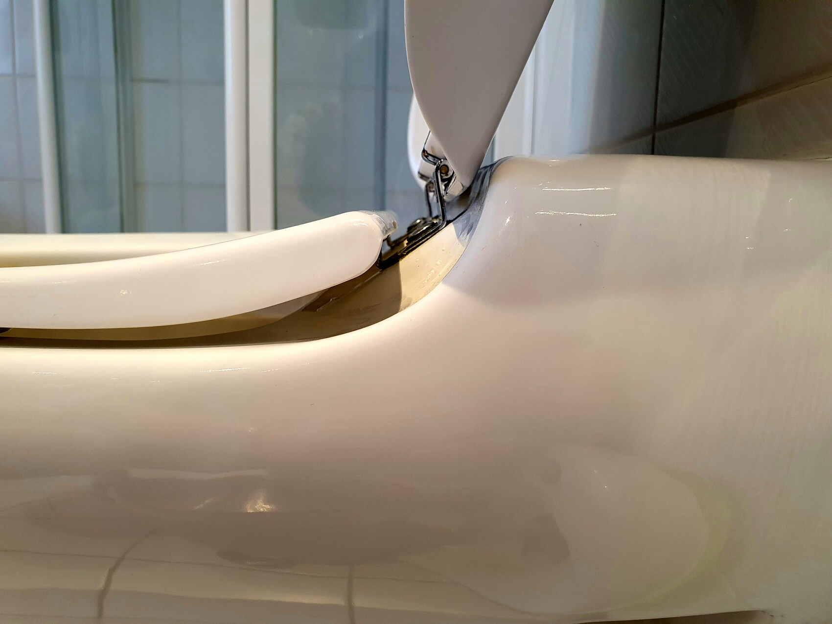 Nahaufnahme einer weißen Toilette mit offenem Deckel und Metall-Scharnier